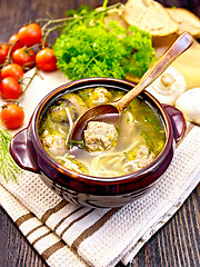 Image showing Soup with meatballs and spoon in clay bowl on dark board