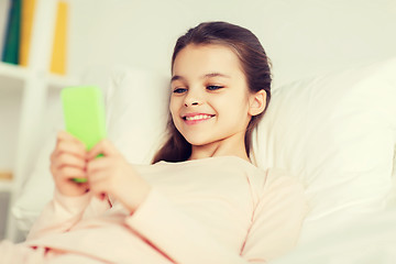 Image showing happy girl lying in bed with smartphone at home