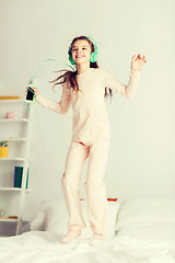 Image showing girl jumping on bed with smartphone and headphones