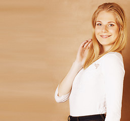 Image showing young cool blong teenage girl messed with her hair smiling on warm brown background, lifestyle people concept