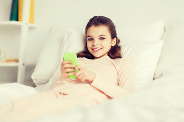 Image showing happy girl lying in bed with smartphone at home