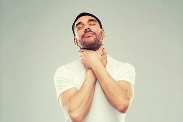 Image showing young man choking himself over gray background