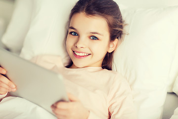 Image showing happy girl lying in bed with tablet pc at home