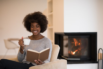 Image showing black woman reading book  in front of fireplace