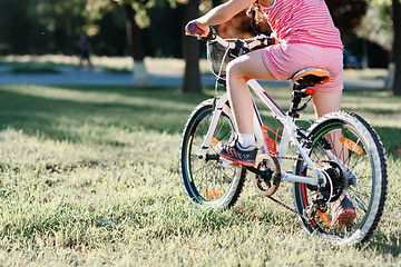 Image showing Little brunette girl riding bicycle in the park at sunset