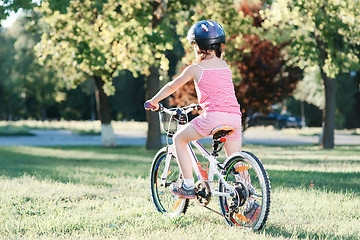 Image showing Little brunette girl riding bicycle in the park at sunset