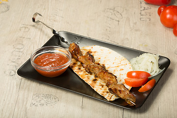 Image showing shashlik. kebab skewer, black rectangular plate. sauce and onions