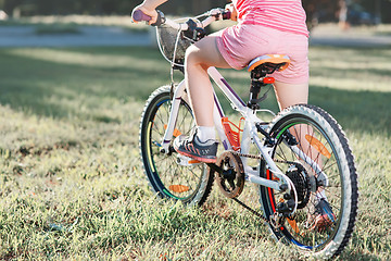 Image showing Little brunette girl riding bicycle in the park at sunset