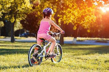 Image showing child girl riding bicycle on summer sunset in the park.