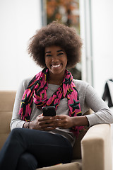 Image showing black woman sitting on sofa and using mobile phone