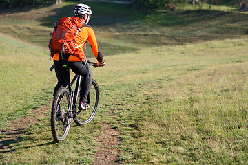 Image showing Young man traveler riding on bicycle with red backpack