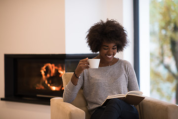 Image showing black woman reading book  in front of fireplace