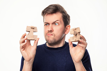 Image showing Attractive 25 year old business man looking confused at wooden puzzle.