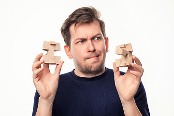 Image showing Attractive 25 year old business man looking confused at wooden puzzle.