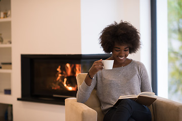 Image showing black woman reading book  in front of fireplace