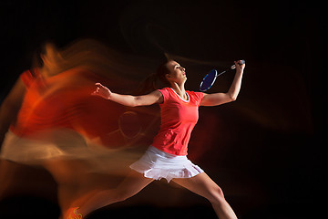 Image showing Young woman playing badminton over black background