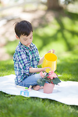 Image showing Mixed Race Young Boy Watering His Potted Flowers Outside On The 