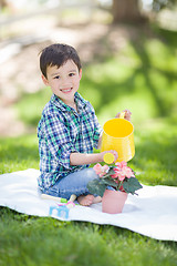 Image showing Mixed Race Young Boy Watering His Potted Flowers Outside On The 