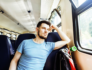 Image showing young pretty modern hipster guy traveller on train with skateboard alone, lifestyle vacation people concept close up smiling cool