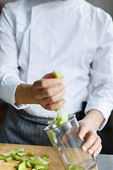 Image showing Crop hands pouring cut celery in container