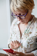 Image showing Mature female in glasses using smartphone