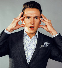 Image showing young pretty business man standing on grey background, modern hairstyle, gesturing emotional