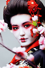 Image showing young pretty geisha in black kimono among sakura, asian ethno close up