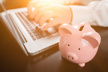 Image showing Piggy Bank Near Male Hands Typing on Laptop Computer.