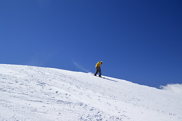 Image showing Snowboarder downhill on off-piste slope and blue clear sky
