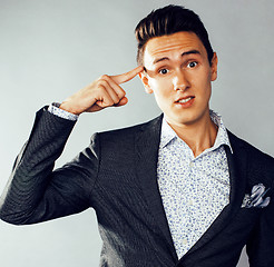 Image showing young pretty business man standing on grey background, modern hairstyle, gesturing emotional