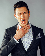 Image showing young pretty business man standing on grey background, modern hairstyle, gesturing emotional