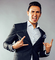 Image showing young pretty business man standing on grey background, modern hairstyle, gesturing emotional