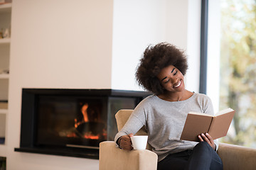 Image showing black woman reading book  in front of fireplace