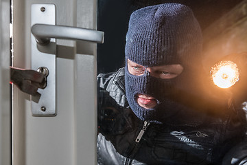 Image showing Masked burglar holding flashlight while trying to break window l