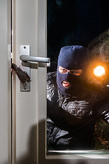 Image showing Masked intruder holding torch while trying to open window with c