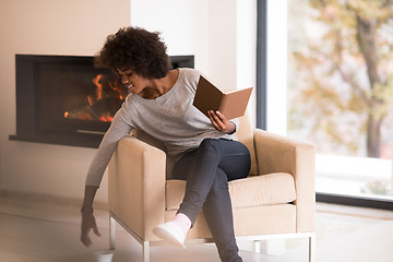 Image showing black woman reading book  in front of fireplace