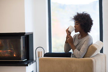 Image showing black woman drinking coffee in front of fireplace