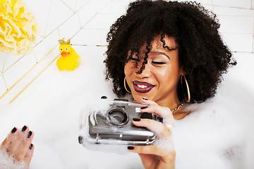 Image showing young afro-american teen girl laying in bath with foam, wearing 