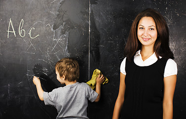 Image showing little cute boy with young teacher in classroom studying at blac