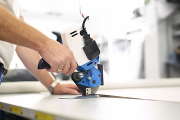 Image showing Cutting room. Knife, table punching fabric. Cutting the fabric, sewing work.