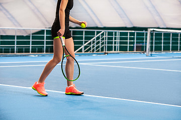 Image showing Legs of young girl in a closed tennis court with ball and racket