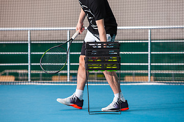 Image showing Legs of man in a closed tennis court with ball and racket