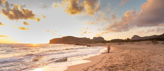 Image showing Woman walking on sandy beach at sunset.