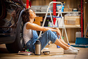 Image showing woman a car mechanic sits in a blue overall in a garage near a c