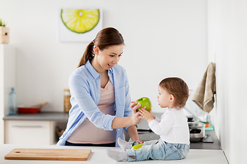 Image showing mother giving green apple to baby at home kitchen