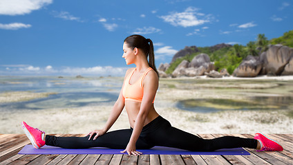 Image showing smiling woman doing splits on mat over beach