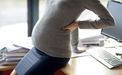 Image showing pregnant businesswoman sitting on table at office