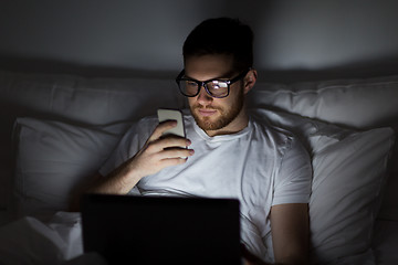 Image showing man with laptop and smartphone at night in bed