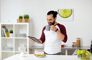 Image showing man with tablet pc eating at home kitchen