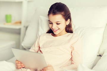 Image showing happy girl lying in bed with tablet pc at home